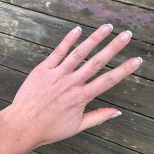 Hand with painted French manicure pink and white on a wooden surface